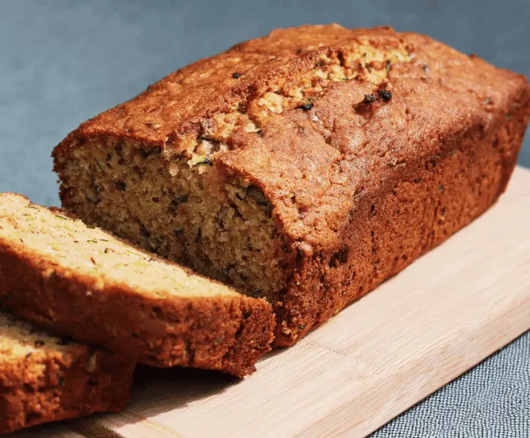 Delicious bakery-style zucchini bread with golden crust and moist interior, topped with shredded zucchini and a sprinkle of cinnamon, perfect for breakfast or snacks