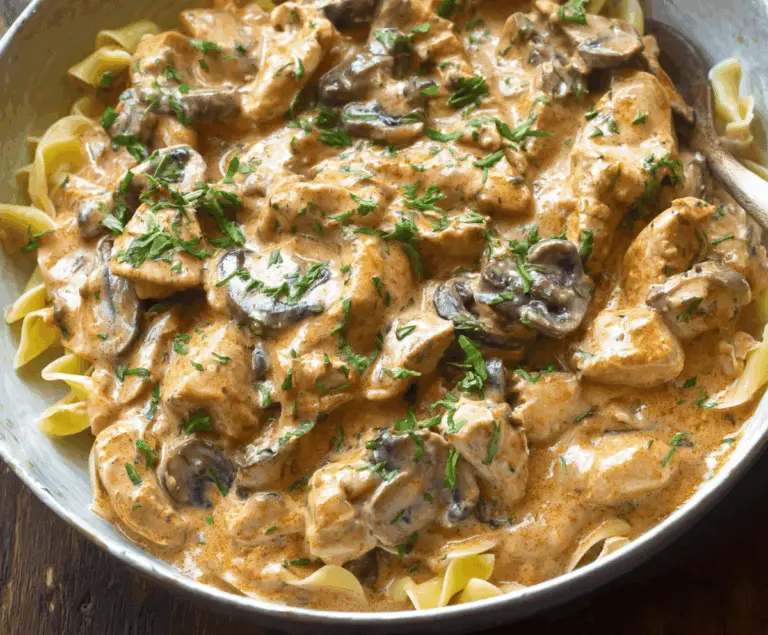 Creamy Chicken Stroganoff served over noodles with fresh herbs and vegetables.
