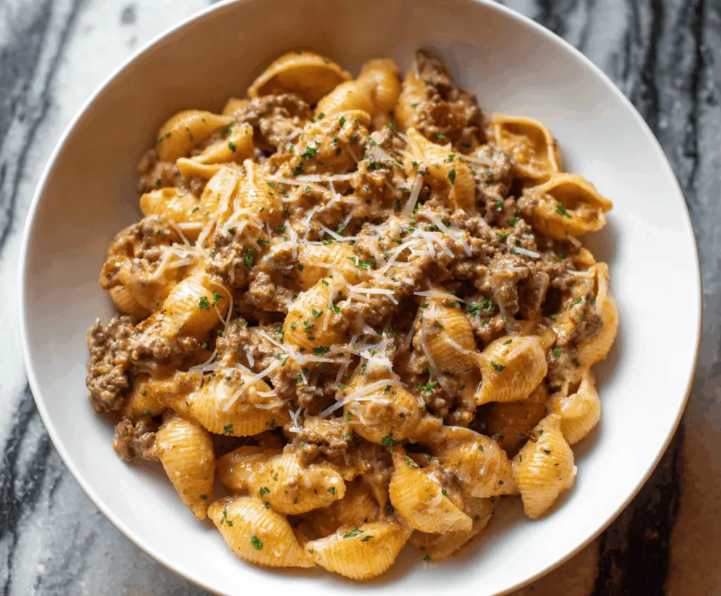 Delicious creamy beef and shell pasta dish topped with melted cheese and fresh herbs, served on a white plate