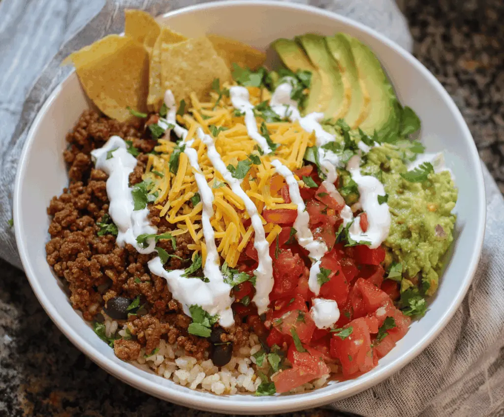 Delicious ground beef burrito bowl with rice, black beans, corn, fresh salsa, and shredded cheese served in a bowl