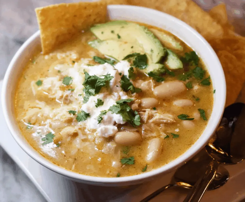 A bowl of creamy white bean enchilada soup garnished with fresh cilantro and shredded cheese, served with tortilla chips on the side.