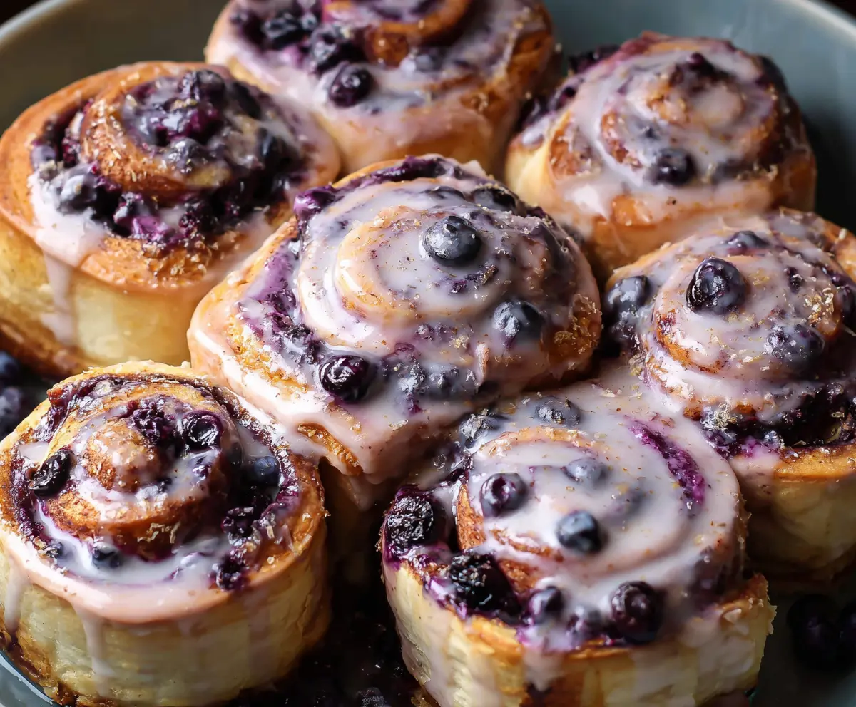 Delicious blueberry cinnamon rolls topped with icing on a white plate, perfect for breakfast or brunch.