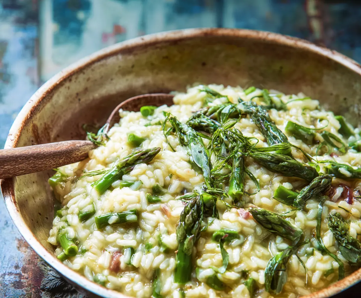 Creamy asparagus risotto garnished with fresh herbs on a white plate.